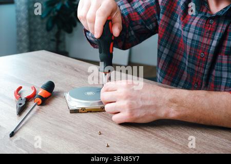 Male engineer repairman disassembles computer hard drive with a screwdriver. Concept of repairing, service, electronics and technology of computer. Stock Photo