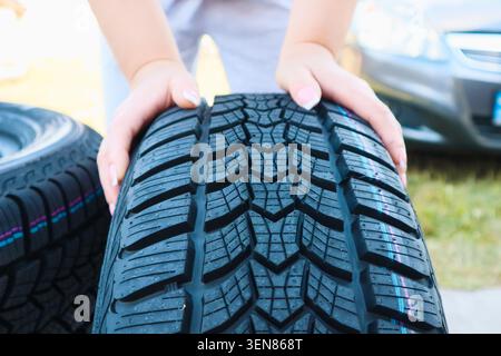 Woman putting hand on new wheel tire. Female holding a tire and standing next to a piles of tires. Auto car repair service Stock Photo