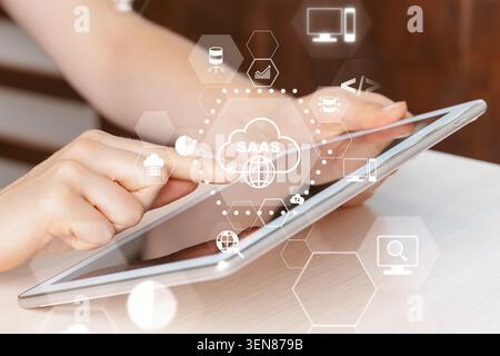 Hands interact with a tablet displaying SaaS icons and cloud symbols in a modern workspace Stock Photo
