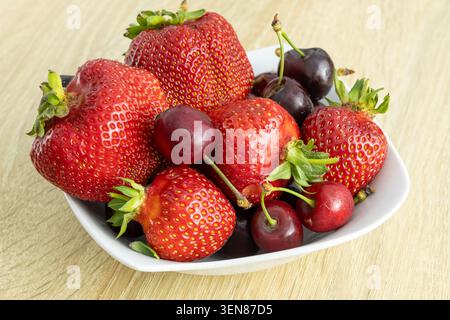 Huge, funny shaped strawberries and sweet cherries on a white plate on the table Stock Photo