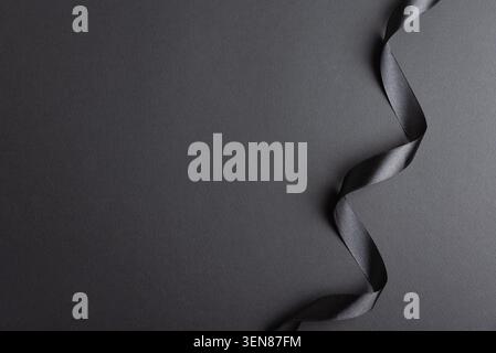 Black satin ribbon displaying a wavy, elegant border on a textured dark grayscale background, creating a luxurious and sophisticated visual ideal for Stock Photo
