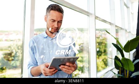 Man using tablet to manage customer data in a bright office with CRM displayed Stock Photo