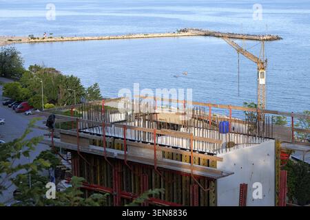 New building project developing on the coastline, showing an unfinished concrete structure with rebar and formwork, with a tower crane standing by the Stock Photo