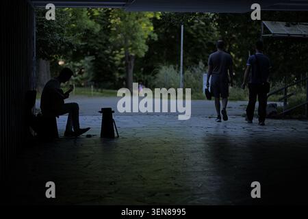 Silhouette of a busker playing an acoustic guitar in a dark underpass tunnel, with people walking by and a green park visible in the background, creat Stock Photo