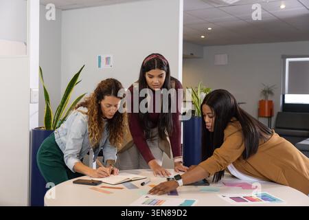 Diverse women colleagues in smart clothes collaborating in office lounge, reviewing color swatches Stock Photo