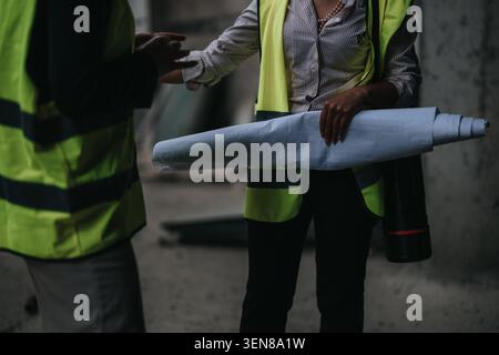 Construction team reviewing blueprints on site with architects and engineers in safety vests Stock Photo