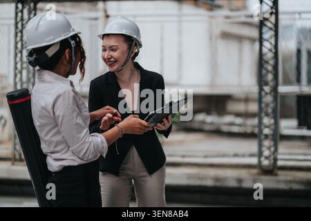 Two female engineers discussing project plans on a construction site while wearing hard hats Stock Photo