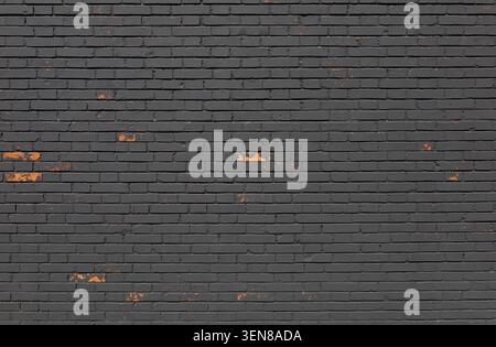 Weathered painted black brick wall with spots where the paint has come off, revealing the underlying orange color. Grunge background for copy space. Stock Photo