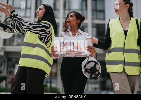 Women engineers discussing construction plans on an urban site while wearing safety vests Stock Photo