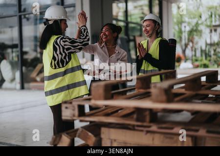 Three female construction workers in hard hats and safety vests celebrating while reviewing building plans Stock Photo