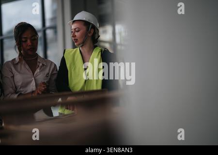 Female construction engineer in hard hat and safety vest consulting colleague over plans on site Stock Photo