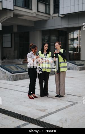 Three female professionals reviewing building plans on site while wearing safety vests and business attire Stock Photo