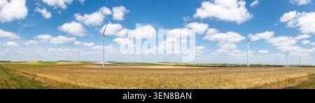 Panoramic view of wind turbines in a wheat field in the French countryside with a blue sky dotted with small white clouds. Concept of renewable energy Stock Photo