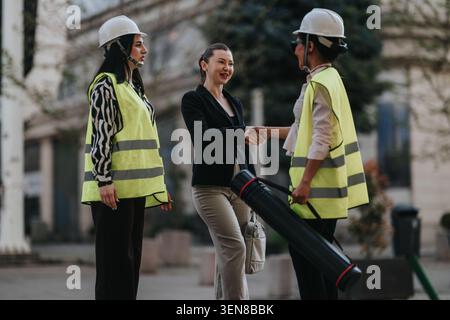 Businesswoman shaking hands with female construction workers in safety vests and helmets outdoors Stock Photo