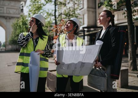 Three female architects and engineers reviewing blueprints at an urban construction site during daytime Stock Photo