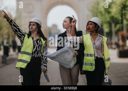 Three female engineers in safety vests and hard hats reviewing blueprints during an urban site visit Stock Photo