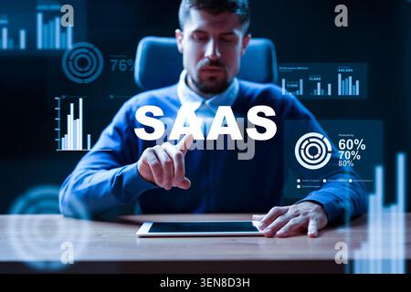 Man interacts with SaaS interface on tablet in office setting during evening hours Stock Photo
