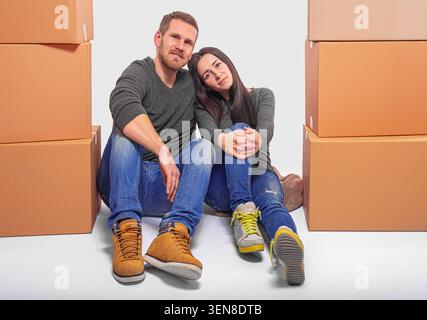 Happy young couple sitting among cardboard boxes. Stock Photo
