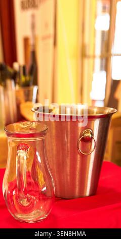 Glass pitcher and metal ice bucket positioned on a red tablecloth, with indistinct background elements indicating a dining or event atmosphere Stock Photo