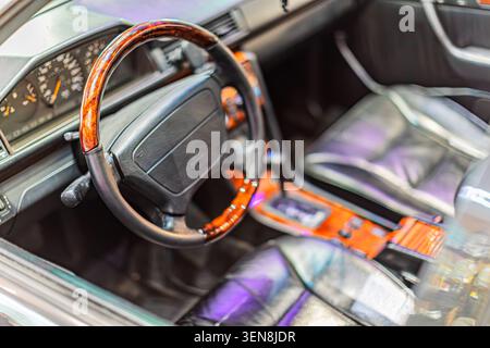 Sophisticated luxury car interior featuring dark leather upholstery and a wooden trimmed steering wheel with worn central panel and modern digital das Stock Photo