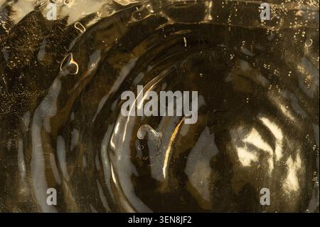 Water creates ripples on a dark surface while sunlight highlights the movement. This scene shows a natural pattern forming in the water. Stock Photo