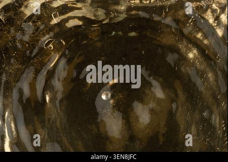 A small object falls into clear water, creating ripples and circles on the surface as the drop disperses and moves outward. Stock Photo
