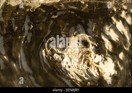 Water forms ripples and swirls, reflecting golden hues in a bright setting. The movement creates interesting patterns on the surface. Stock Photo