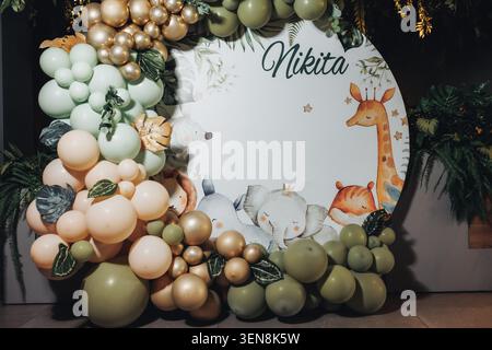 Pastel balloons frame a giraffe-themed birthday backdrop. Green and gold hues create a soft, natural feel. Giraffe, deer, and leaf decorations add whi Stock Photo