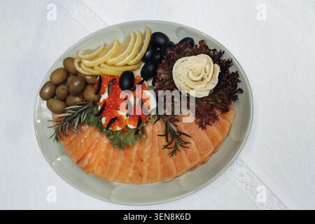 Salmon slices artfully arranged on a plate. Garnished with olives, cheese, and fresh herbs. Rosette of cream adds elegant contrast. Perfect for sophis Stock Photo