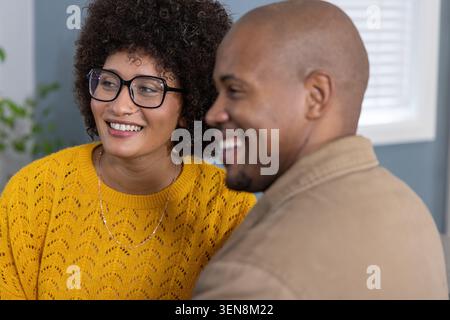 Couple sitting smiling in lounge, woman wearing yellow sweater and glasses, man wearing tan jacket Stock Photo