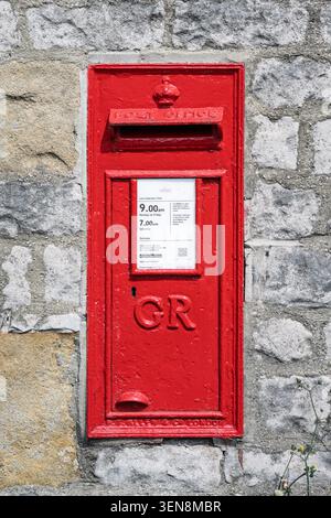 Close-up vertical detail of a historic red George V post box set into a traditional limestone wall in Tideswell village Stock Photo