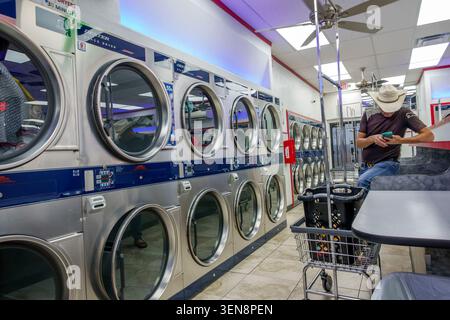 Phoenix Arizona,Coin Less Laundry,laundromat interior,Hispanic man,adult male,cowboy hat,using smartphone,seated customer,Dexter stack dryers,commerci Stock Photo
