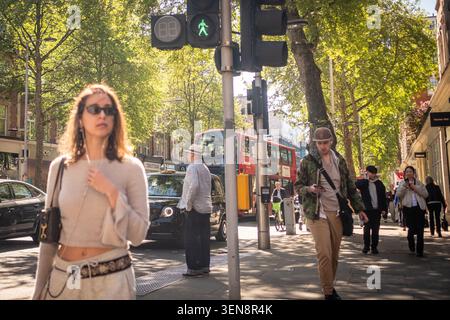 LONDON - APRIL 23, 2026: Kensington High Street – young woman with sunglasses on busy sunny London street with red buses Stock Photo