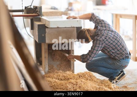 Craftsperson diligently cleaning woodworking machine from wood shavings Stock Photo