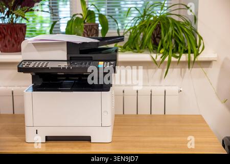 Modern laser printer machine on wooden desk in corporate office. Concept: office printing Stock Photo