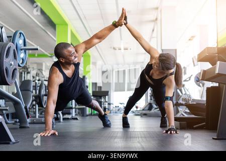Black fitness giving high five while in push-up position on gym Stock Photo