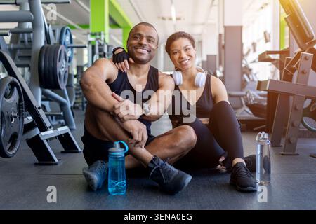 Black sitting together on gym floor after exercise, smiling at camera Stock Photo