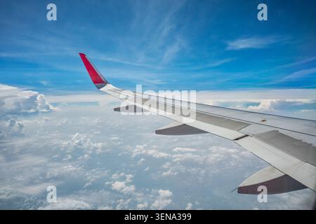 Plane wing flying above the blue sky and clouds from the airplane window of passenger seat. Stock Photo