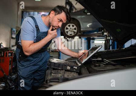 Auto mechanic using a computer to diagnose a car engine problem in a repair shop Stock Photo
