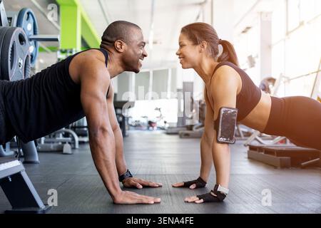Young Black fitness doing push-ups facing each other on gym floor Stock Photo