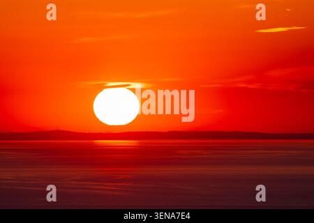 Huge orange sun setting over calm sea and distant horizon Stock Photo