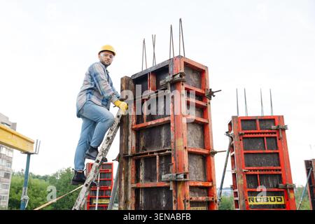 Construction worker in hard hat and safety glasses climbing ladder, setting metal formwork for a reinforced concrete column Stock Photo