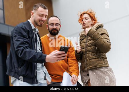Business team shares ideas outside office discussing project on phone and collaborating in a modern urban environment during work hours Stock Photo
