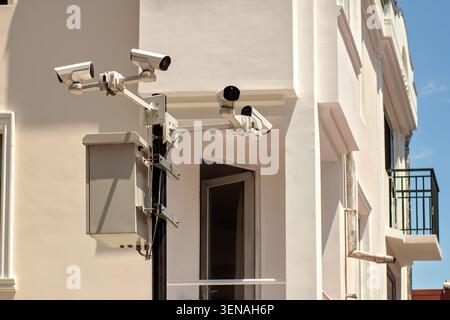 System of four white CCTV security cameras and a control box mounted on a metal pole on the background of a modern residential building facade. Stock Photo