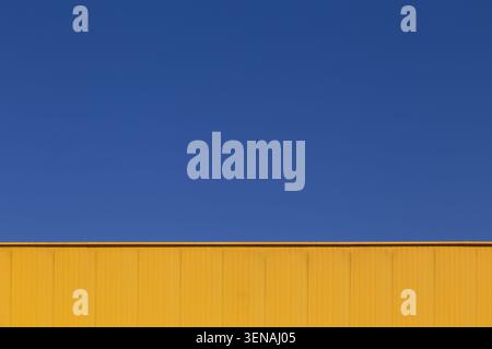 Abstract industrial background with blue sky and yellow warehouse wall Stock Photo