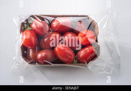 Red datterini tomatoes packaged in a cardboard tray wrapped in plastic for sale in supermarket Stock Photo