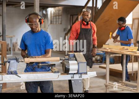 African American instructor and teenage students using lathe, sanding plank in workshop, copy space Stock Photo