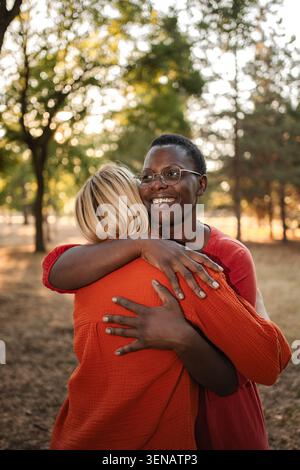 Two smiling female friends hugging each other in a park Stock Photo