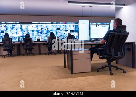 Wide shot of a spacious and modern security control room showing operators working at desks and an extensive multi screen cctv video wall displaying r Stock Photo