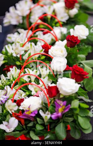 A row of elegant floral arrangements featuring fresh red and white roses, alstroemeria, and purple flowers in gift baskets with red handles. Stock Photo
